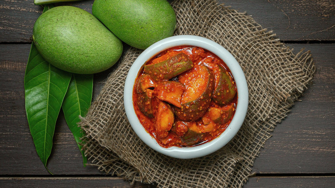 mango pickle or aam ka aachar or achar in a bowl on wooden background theme with raw mangos around that