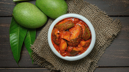 mango pickle or aam ka aachar or achar in a bowl on wooden background theme with raw mangos around that